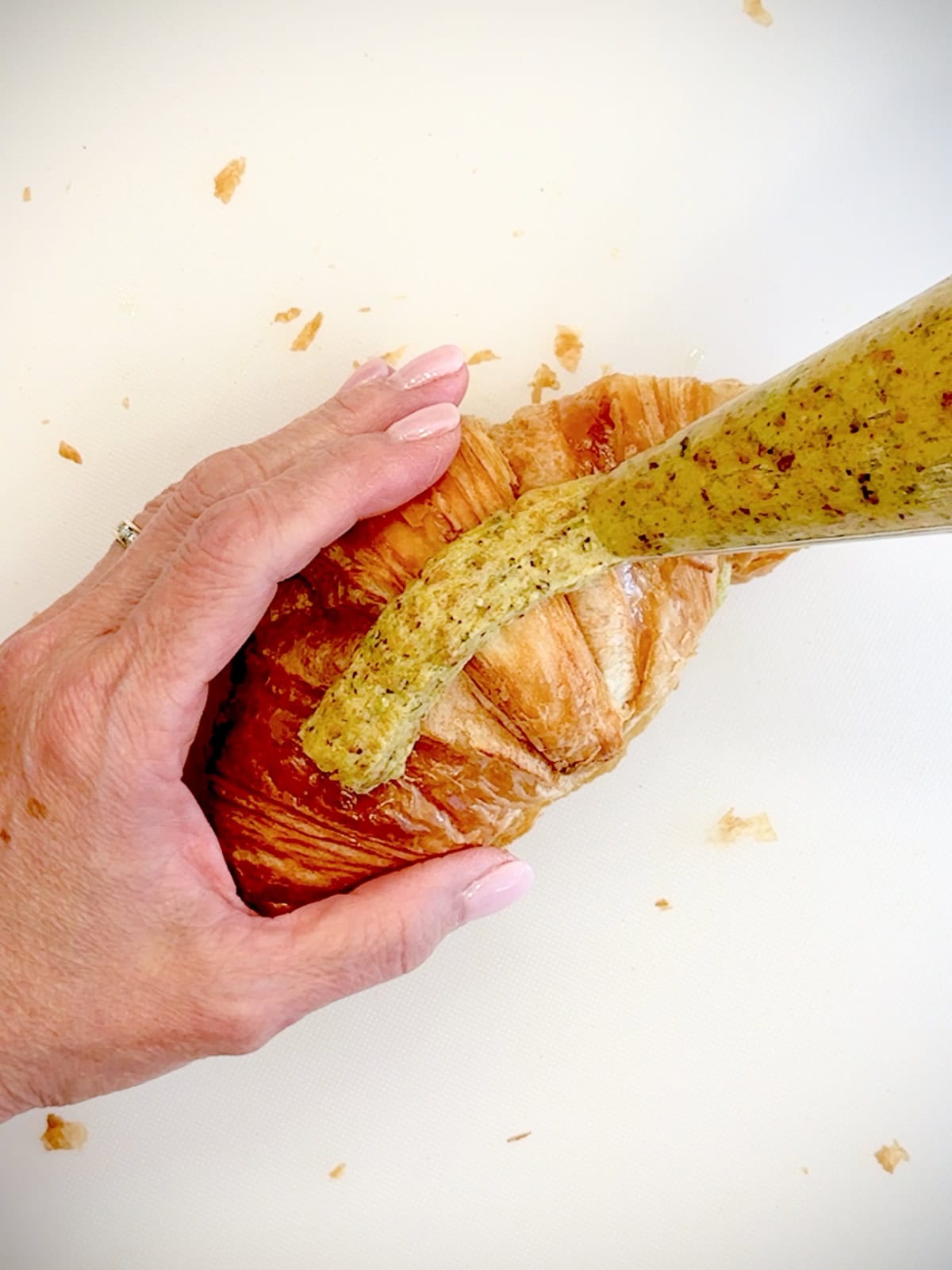 Piping pistachio cream on top of a croissant.