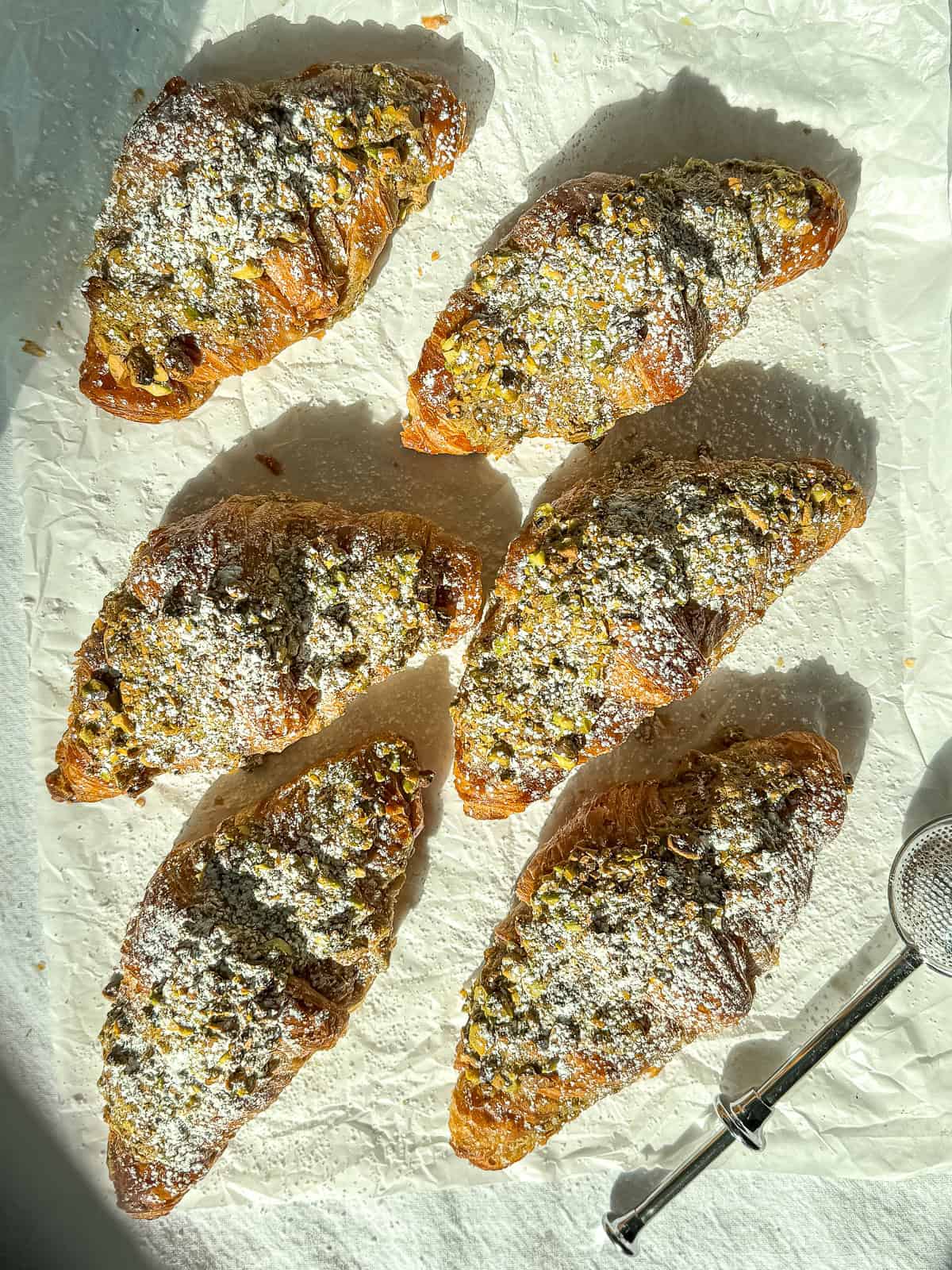 Pistachio filled croissants that have been dusted with sugar on parchment paper.