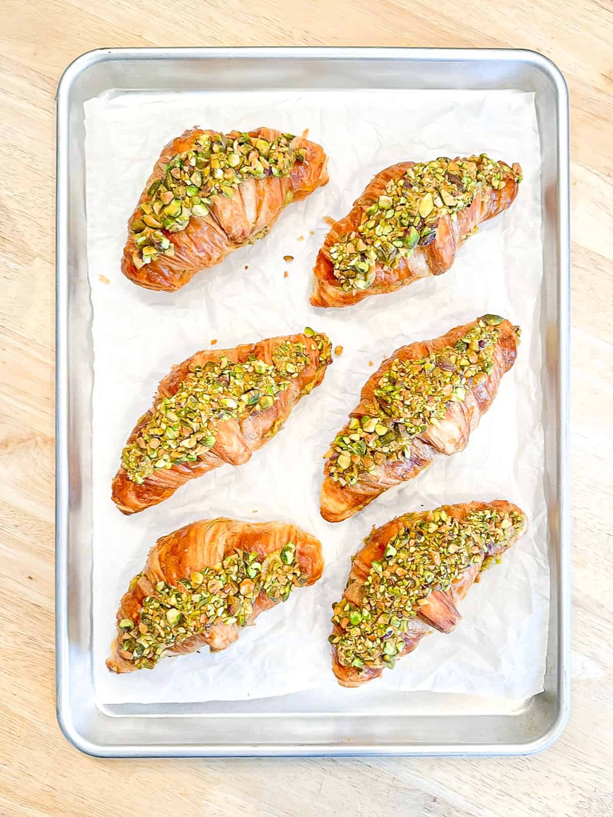 Unbaked pistachio filled croissants on a sheet tray.