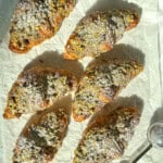 Pistachio filled croissants that have been dusted with sugar on parchment paper.
