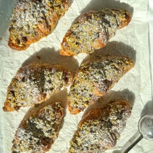 Pistachio filled croissants that have been dusted with sugar on parchment paper.