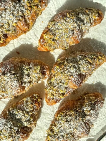 Pistachio filled croissants that have been dusted with sugar on parchment paper.