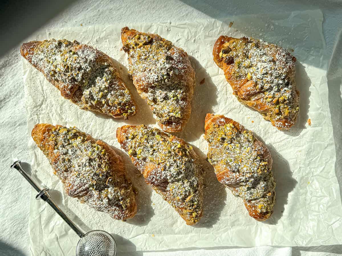 Pistachio filled croissants that have been dusted with sugar on parchment paper.