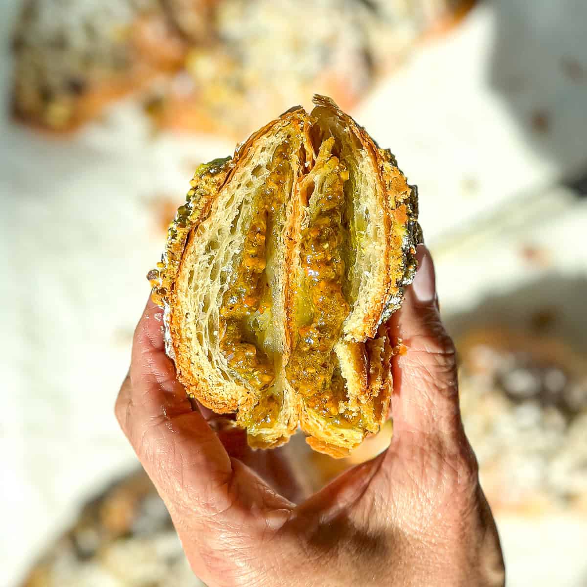 The author's hand holding a pistachio filled croissant that is cut in half to reveal the interior.