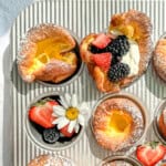 Muffin tin popovers in a muffin pan with cream and berries and decorative flowers.