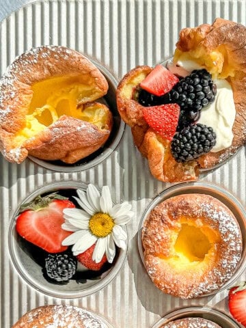 Muffin tin popovers in a muffin pan with cream and berries and decorative flowers.