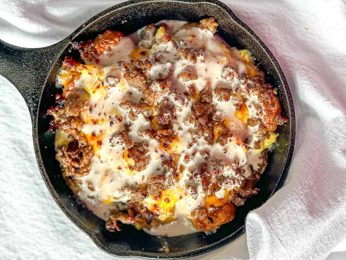 Sausage topped tater tot breakfast skillet in a mini cast iron pan.