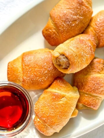 Breakfast pigs in a blanket on a white plate with maple syrup.