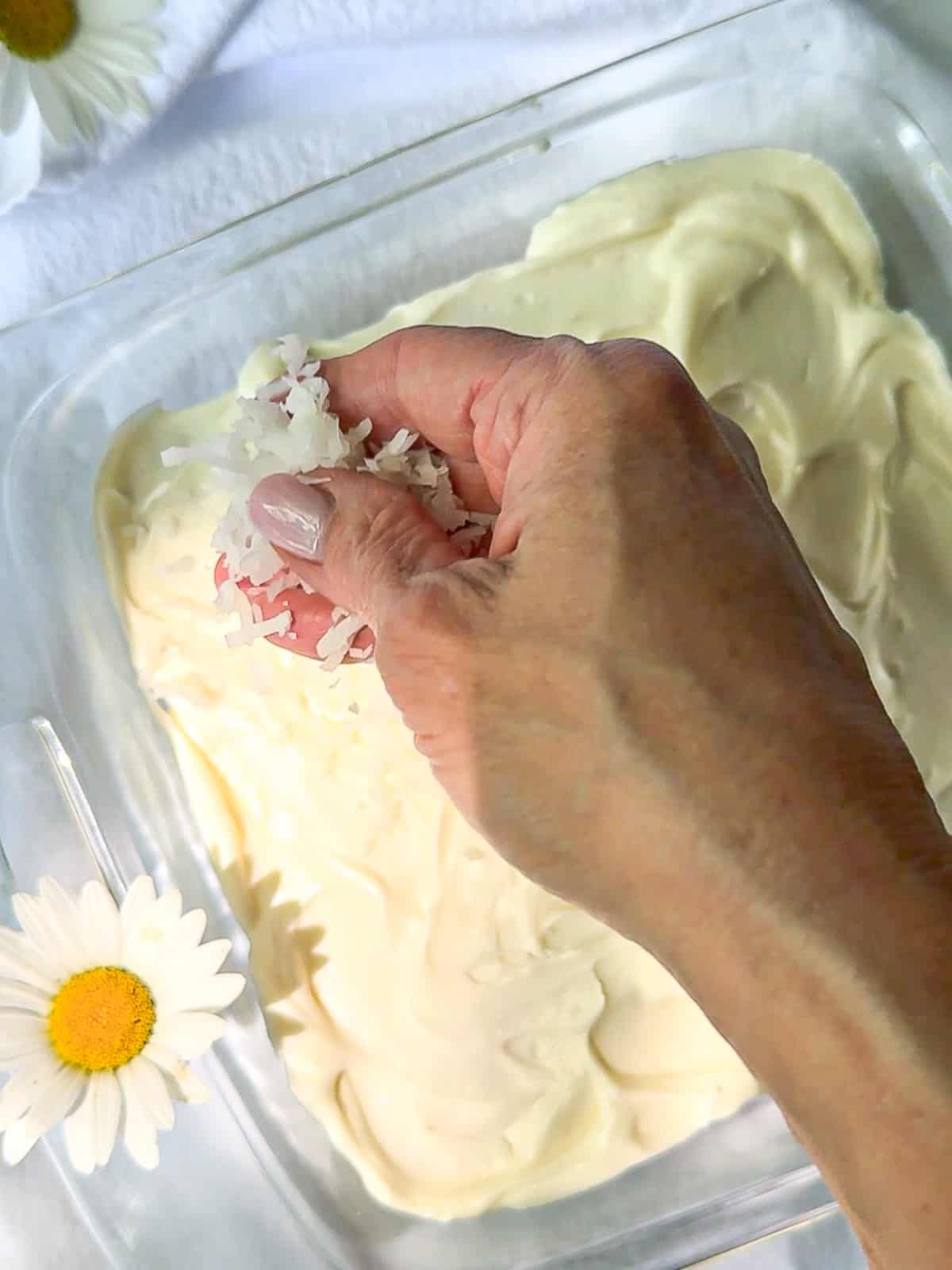 Sprinkling shredded coconut on top of coconut cake.