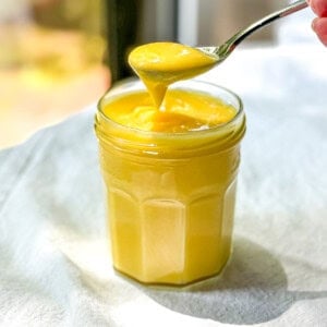 A spoon holding bright yellow easy lemon curd over a jar of more curd.