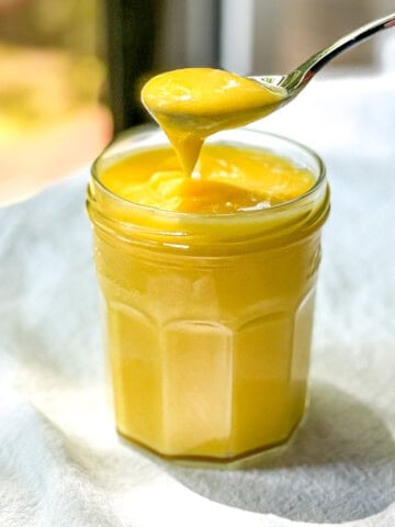 A spoon holding bright yellow easy lemon curd over a jar of more curd.