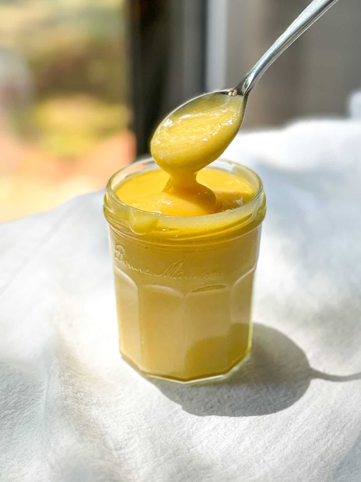 A spoon holding bright yellow easy lemon curd over a jar of more curd.