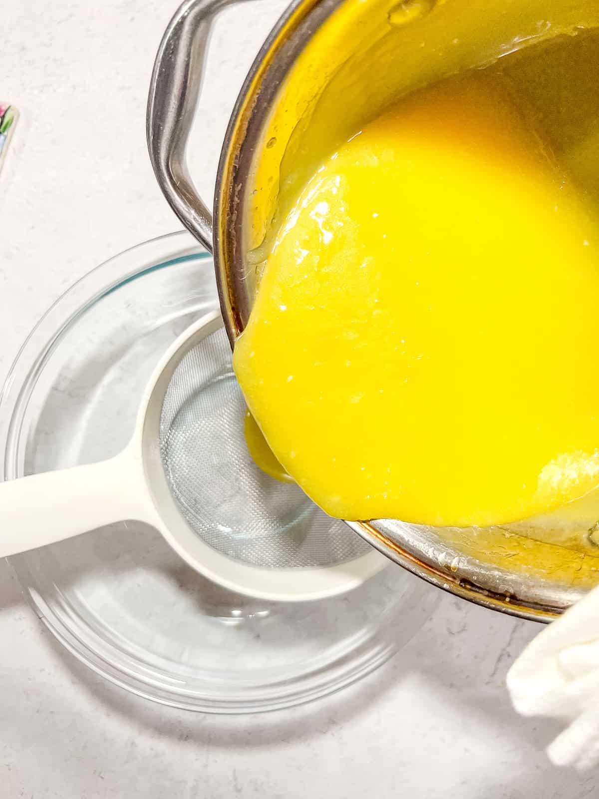 Pouring curd through a wire mesh strainer.