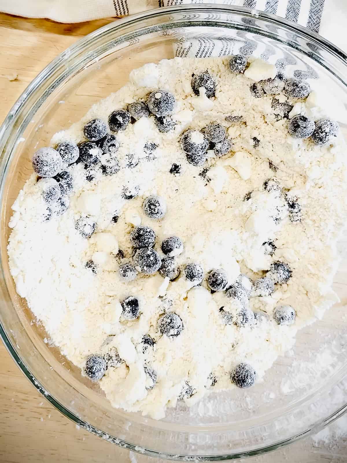 Adding blueberries to blueberry biscuit dry ingredients.