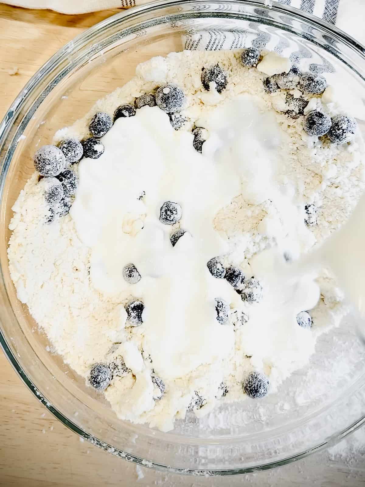 Adding buttermilk to make blueberry biscuits.