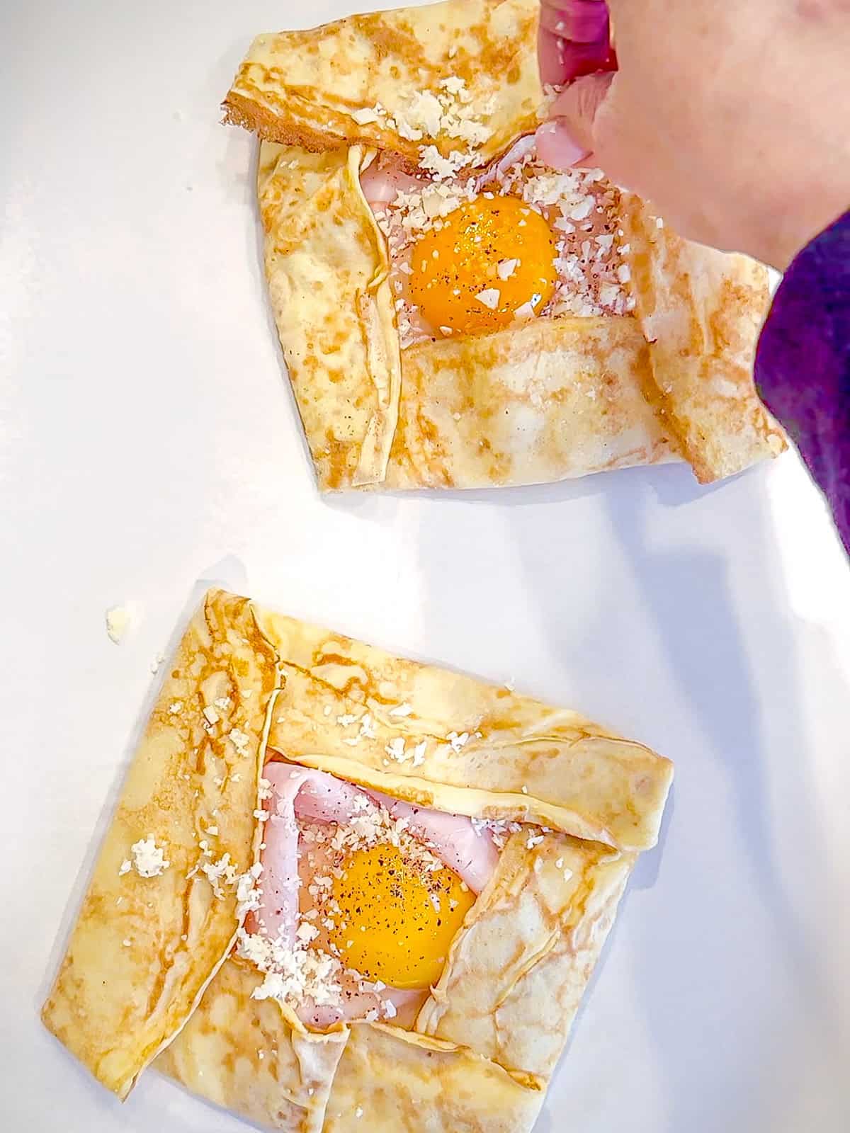 Sprinkling extra cheese on top of ham and egg and cheese crepes.