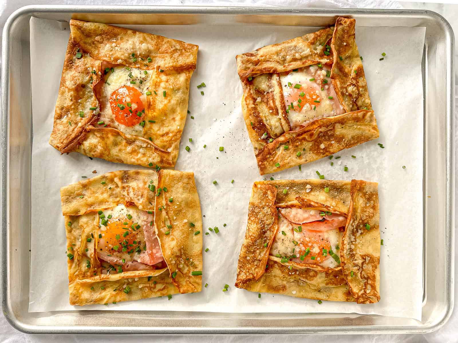 Ham and cheese crepes with eggs on a large sheet pan.