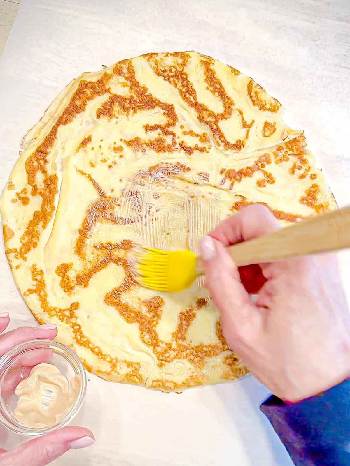 Brushing dijon mustard on the center of a crepe.