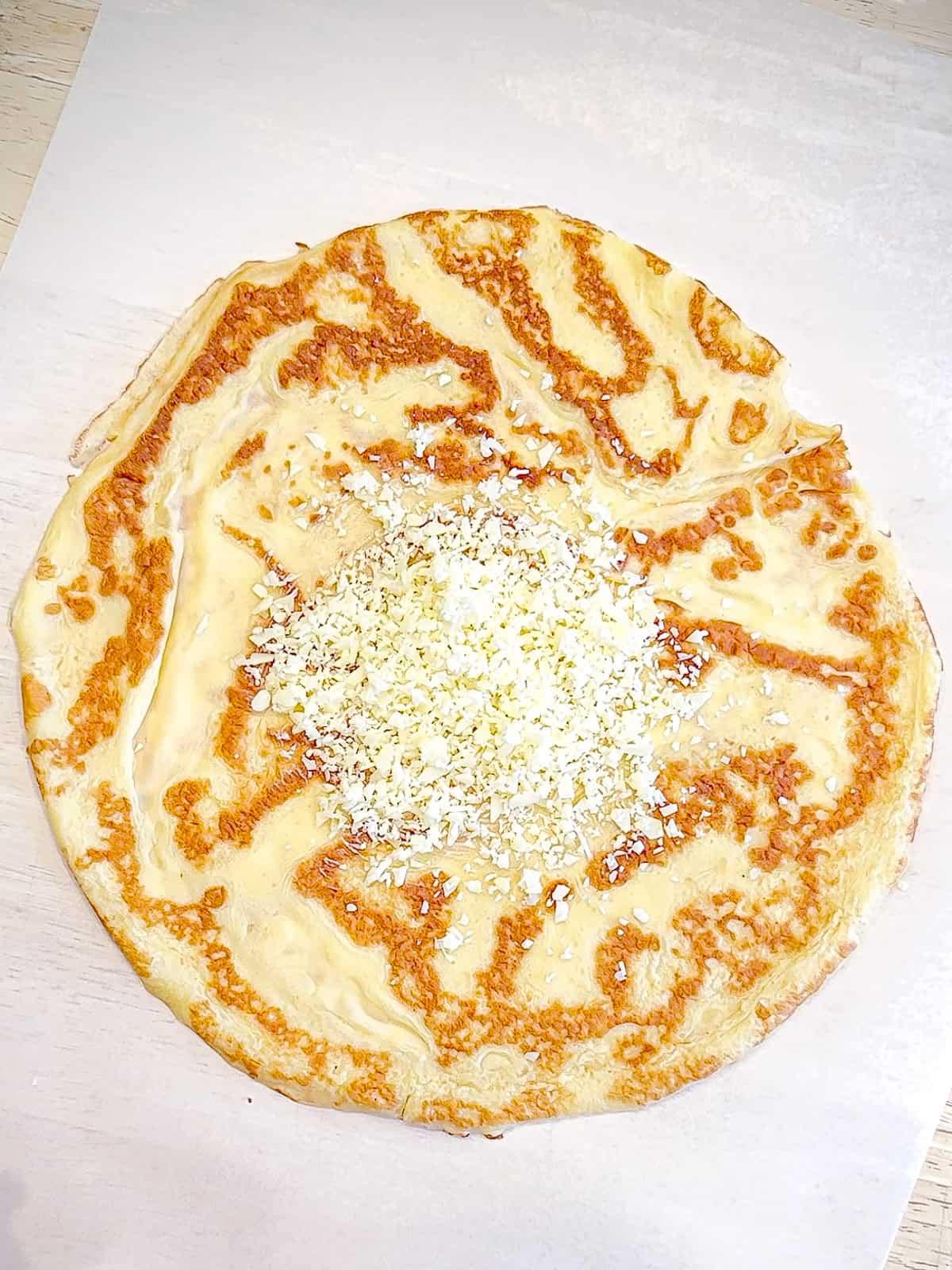 Sprinkling grated swiss cheese on a crepe.