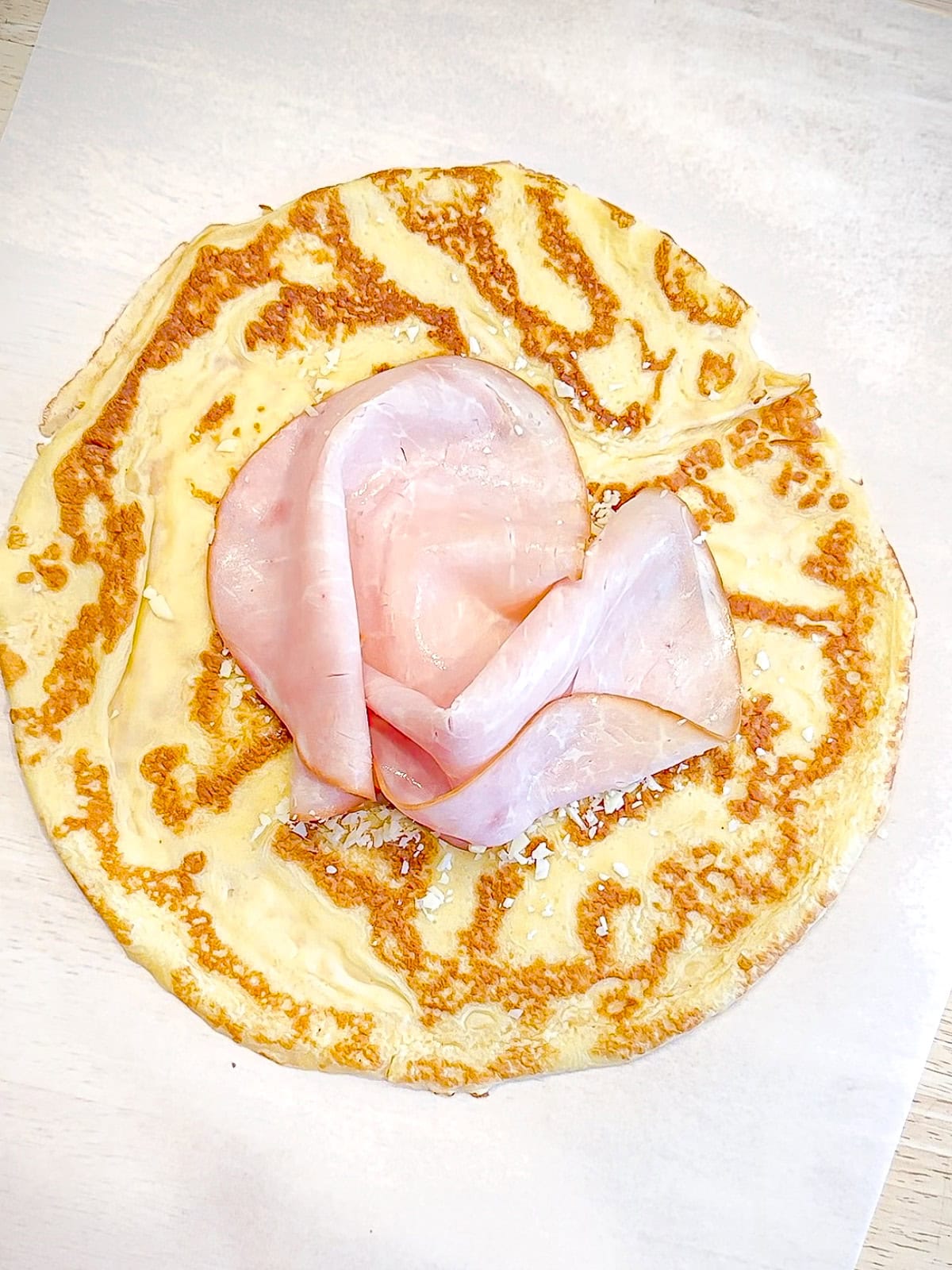 Nestling ham on top of a crepe with grated cheese.