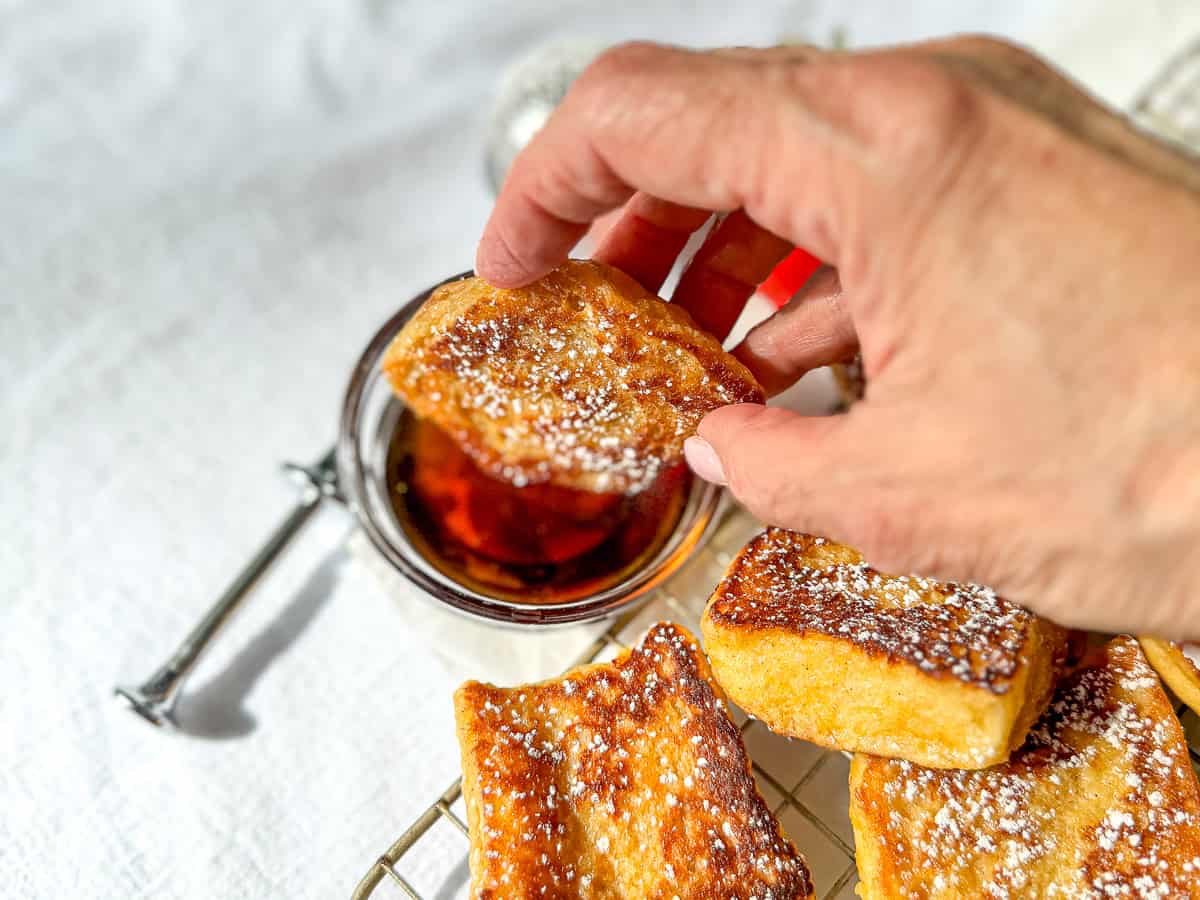 Dipping a piece of Hawaiian bread French toast into a bowl of maple syrup.