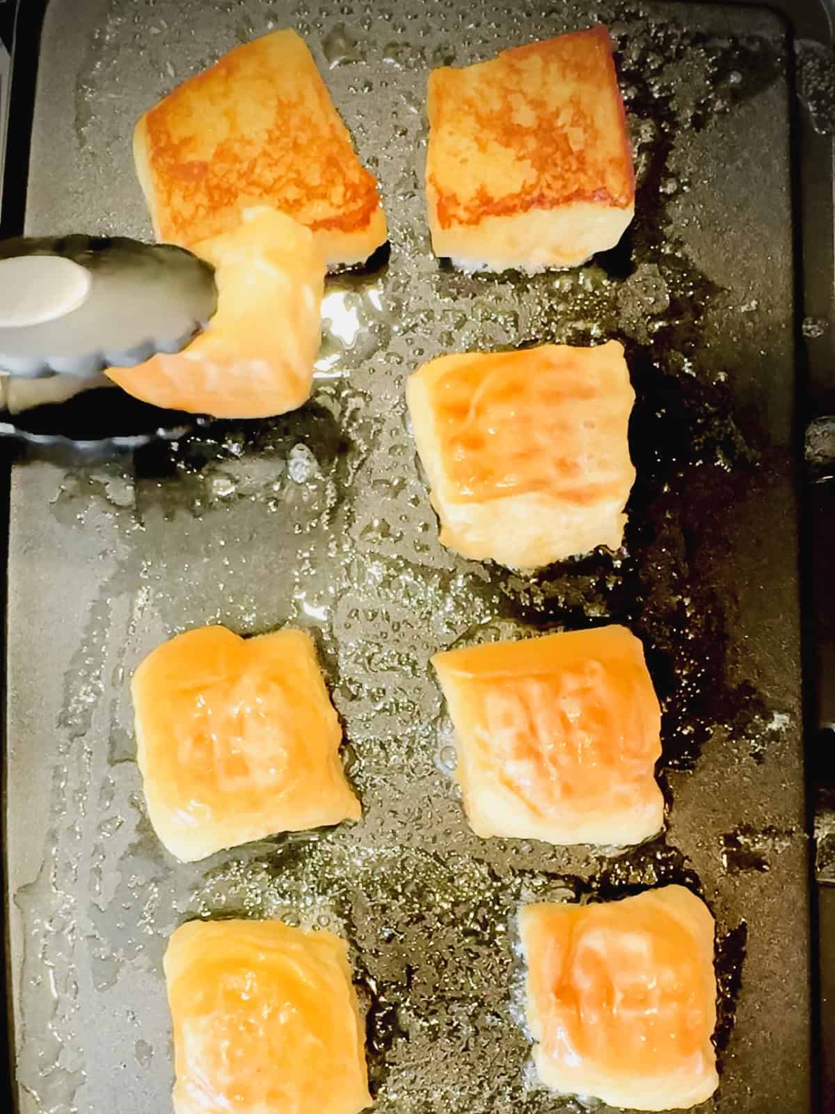 Using tongs to flip Hawaiian bread French toast on a griddle.