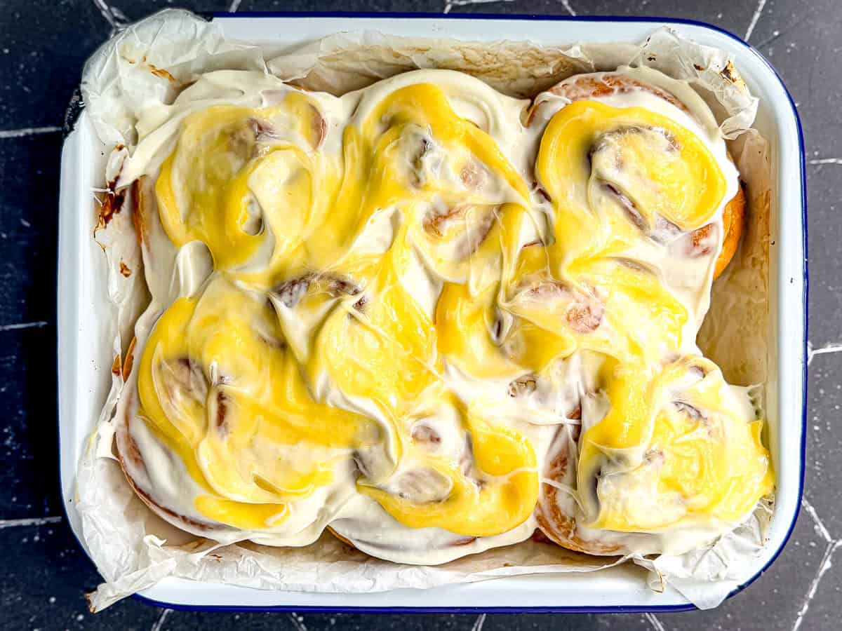 Lemon rolls with cream cheese frosting and lemon curd in a white pan.