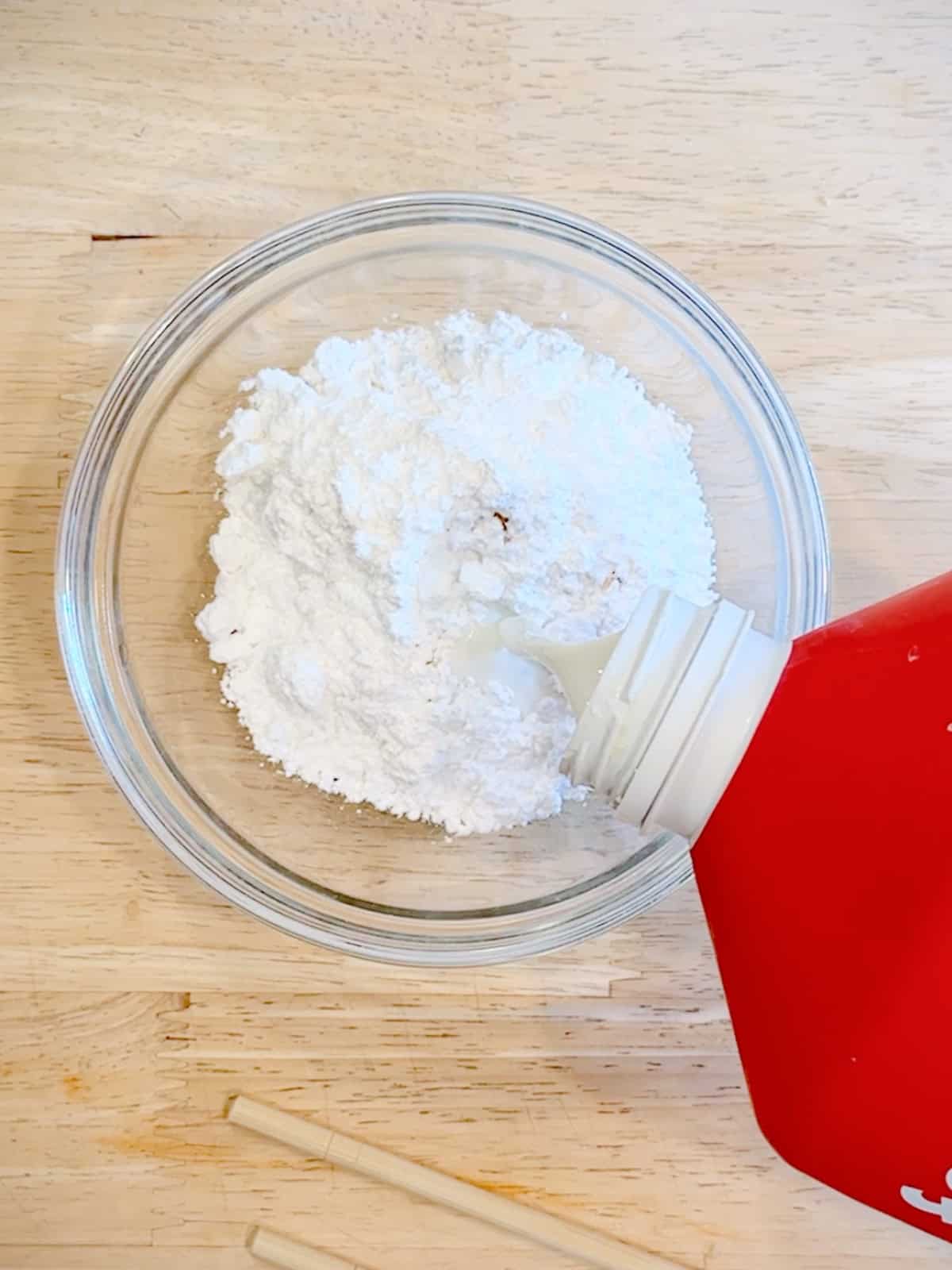Adding milk to powdered sugar to make vanilla glaze.
