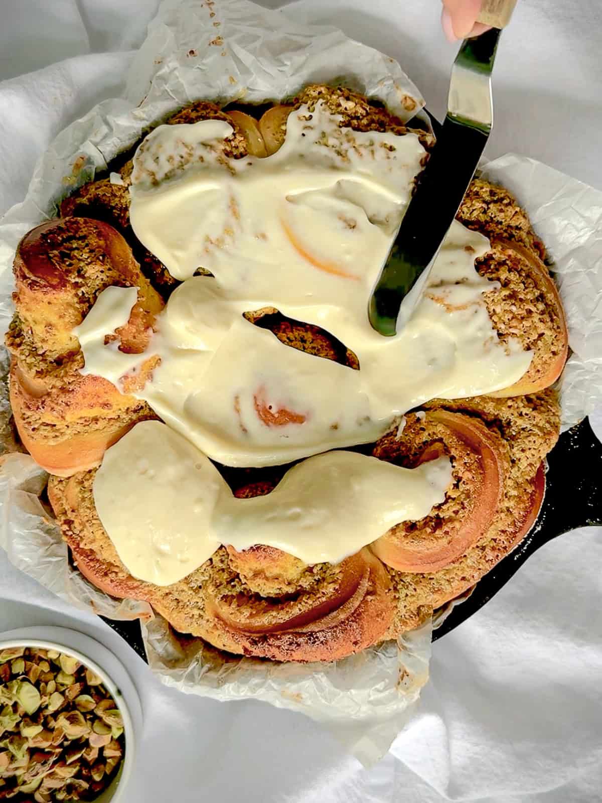 Spreading cream cheese icing onto pistachio rolls.