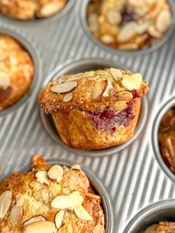 Blackberry muffins with almonds on top in a muffin pan.