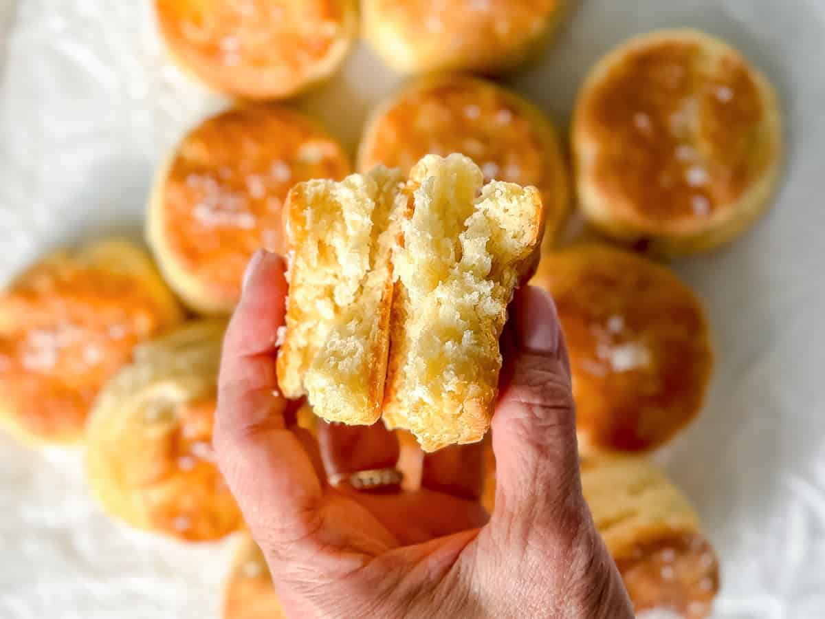 Author's hand holding a homemade biscuit that is broken in half.