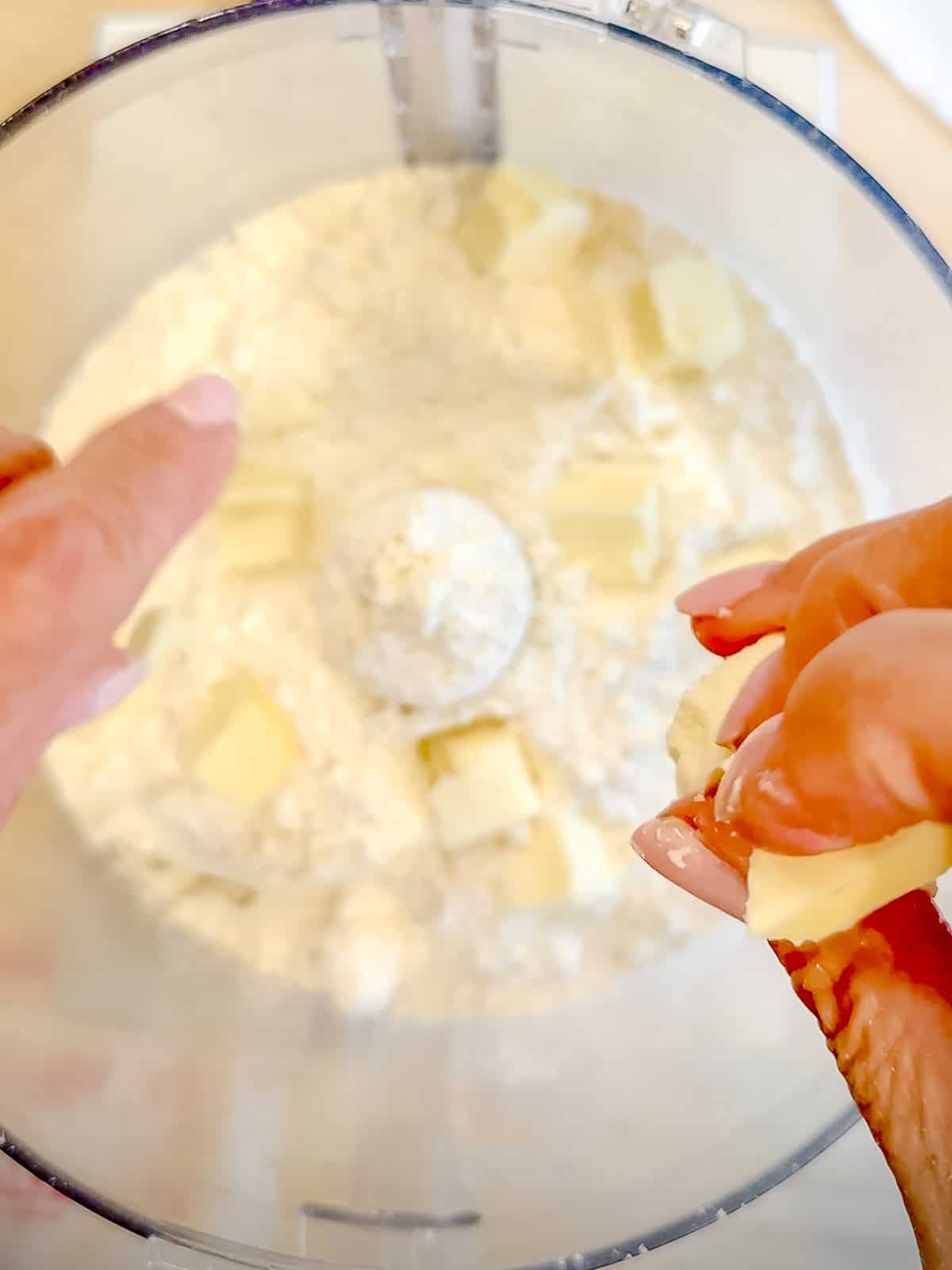 Adding cubes of butter into self rising flour in a food processor.