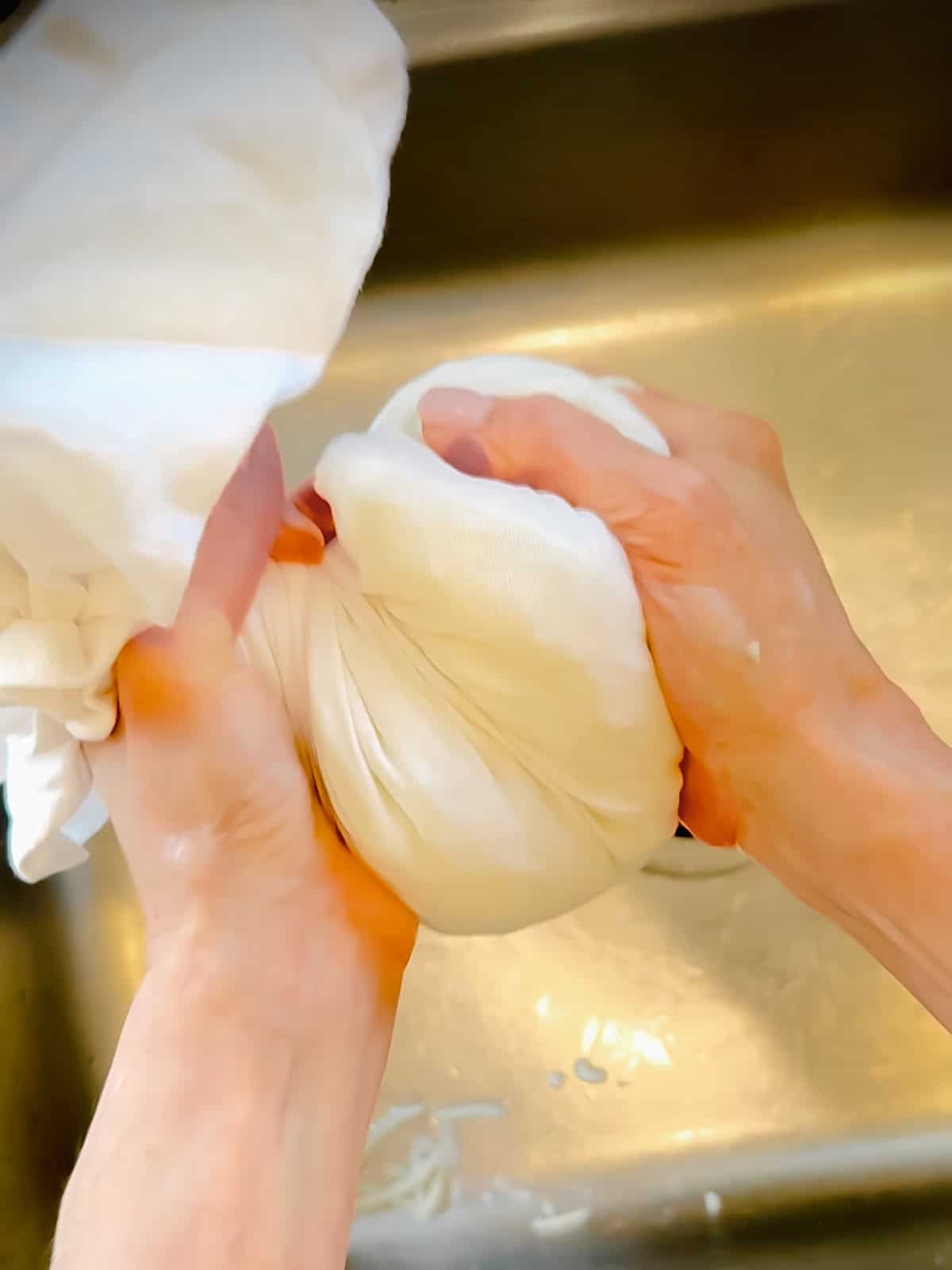 Squeezing shredded potatoes in a white kitchen towel to remove excess liwuid.