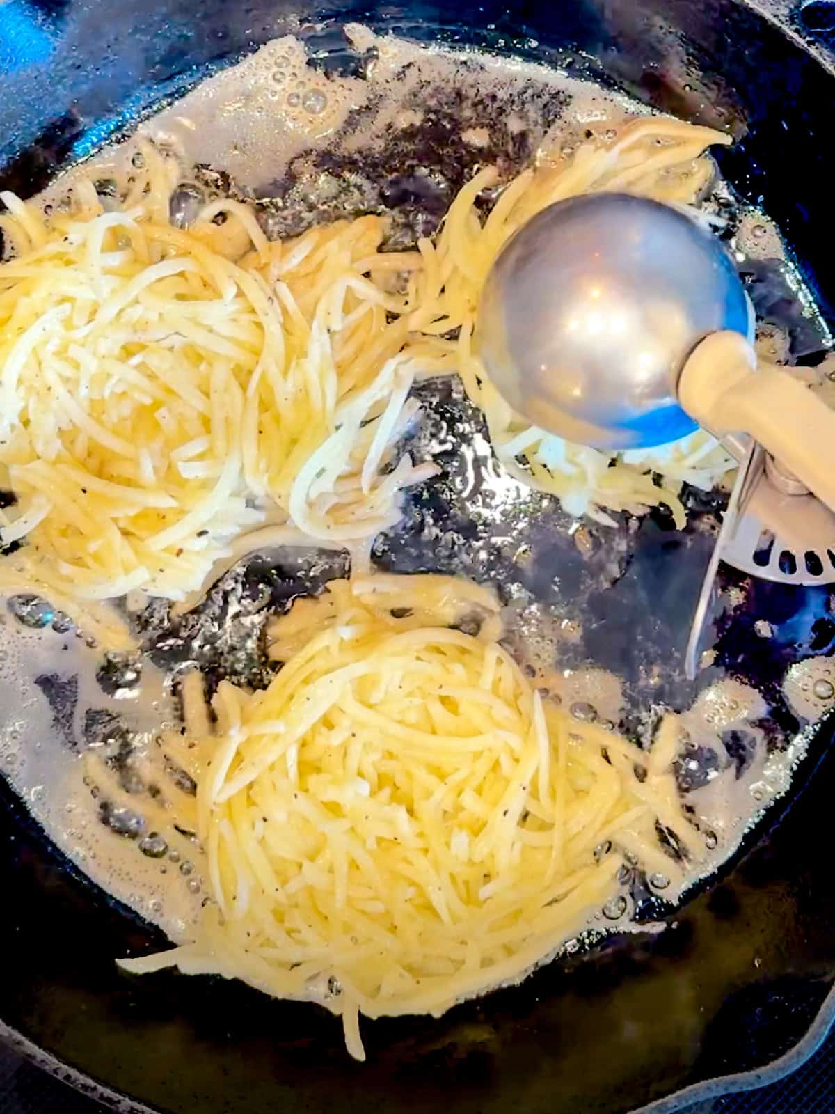 Using a large scoop to portion out shredded potatoes ina cast iron pan.