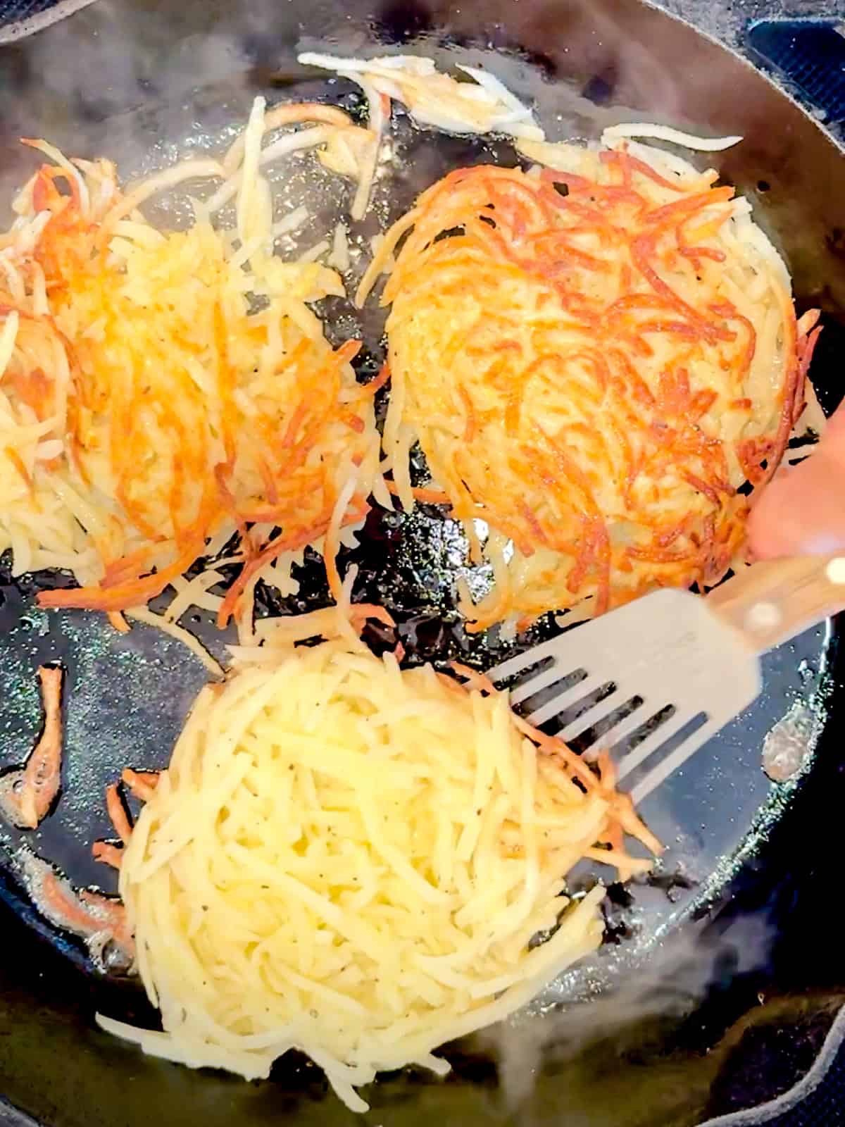 Flipping over hash brown patties in a cast iron pan.