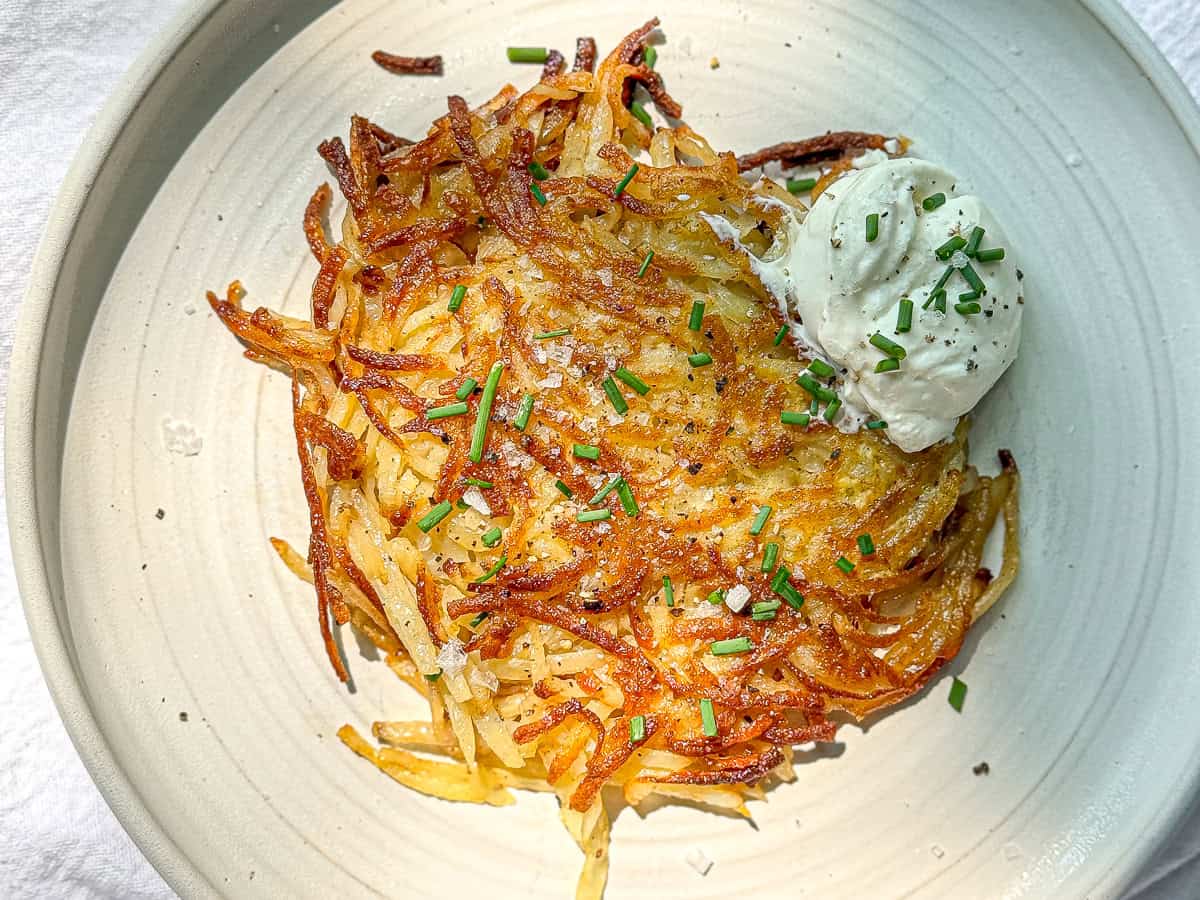 Hash brown patty on a plate with sour cream and chives on the side.