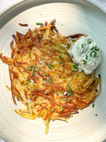 Hash brown patty on a plate with sour cream and chives on the side.