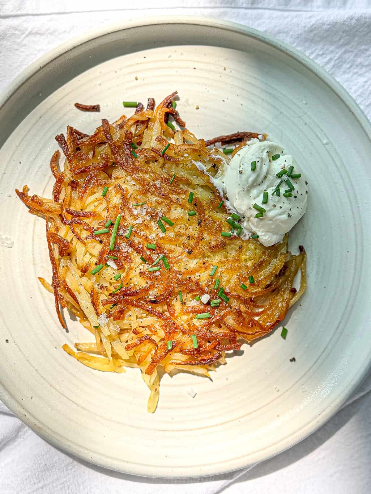 Hash brown patty on a plate with sour cream and chives on the side.