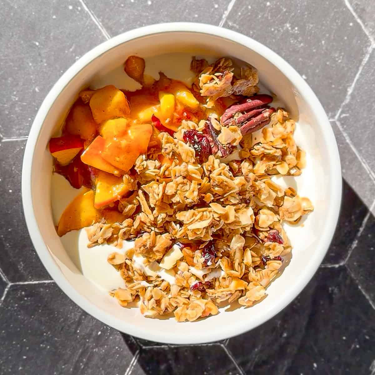 Brown sugar peaches and granola on top of yogurt in a white bowl.
