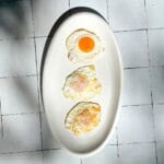 Vertical image of three fried eggs on a white plate.