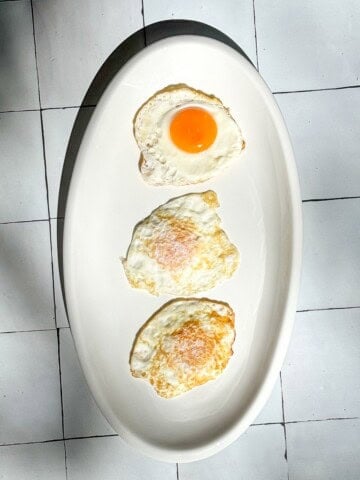 Vertical image of three fried eggs on a white plate.