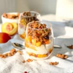 Yogurt and brown sugar peach parfaits topped with granola in small glasses.
