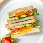 A sliced BLT with egg on a white plate with a tan rim.