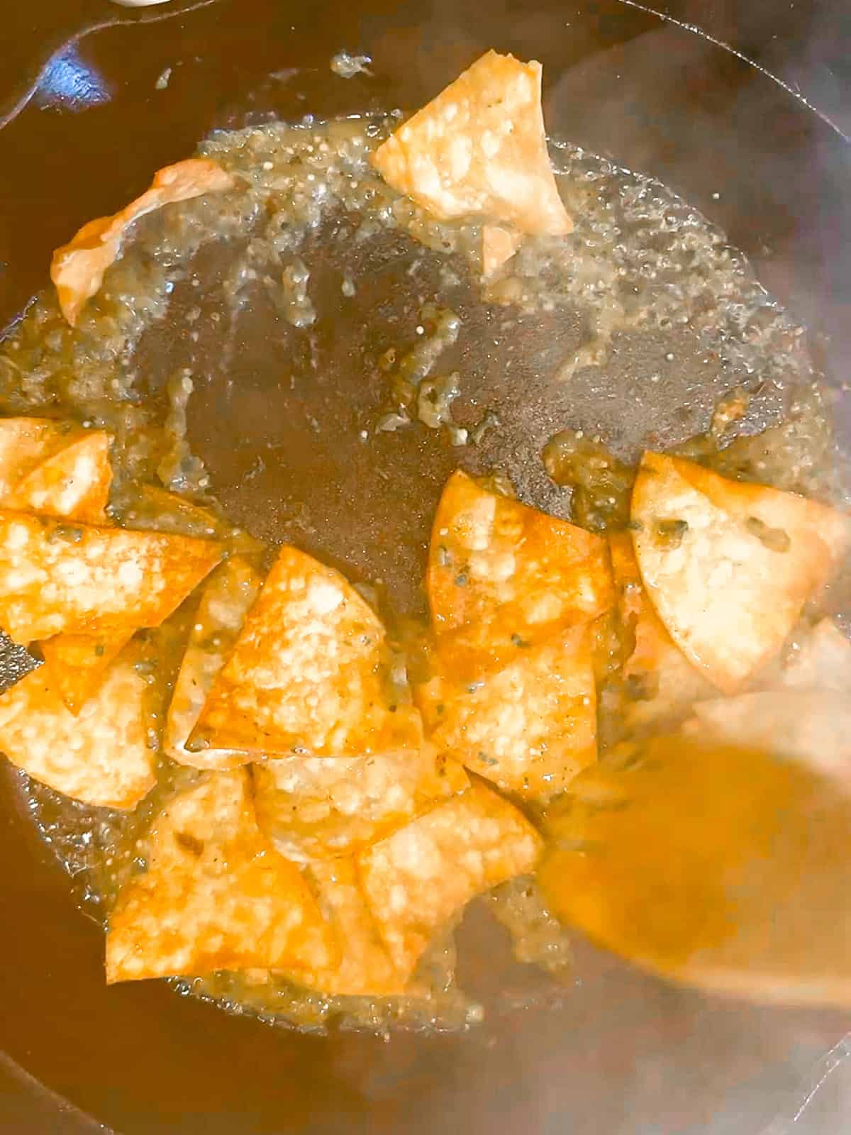 Mixing together tortilla chips and salsa Verde in a cast-iron pan.