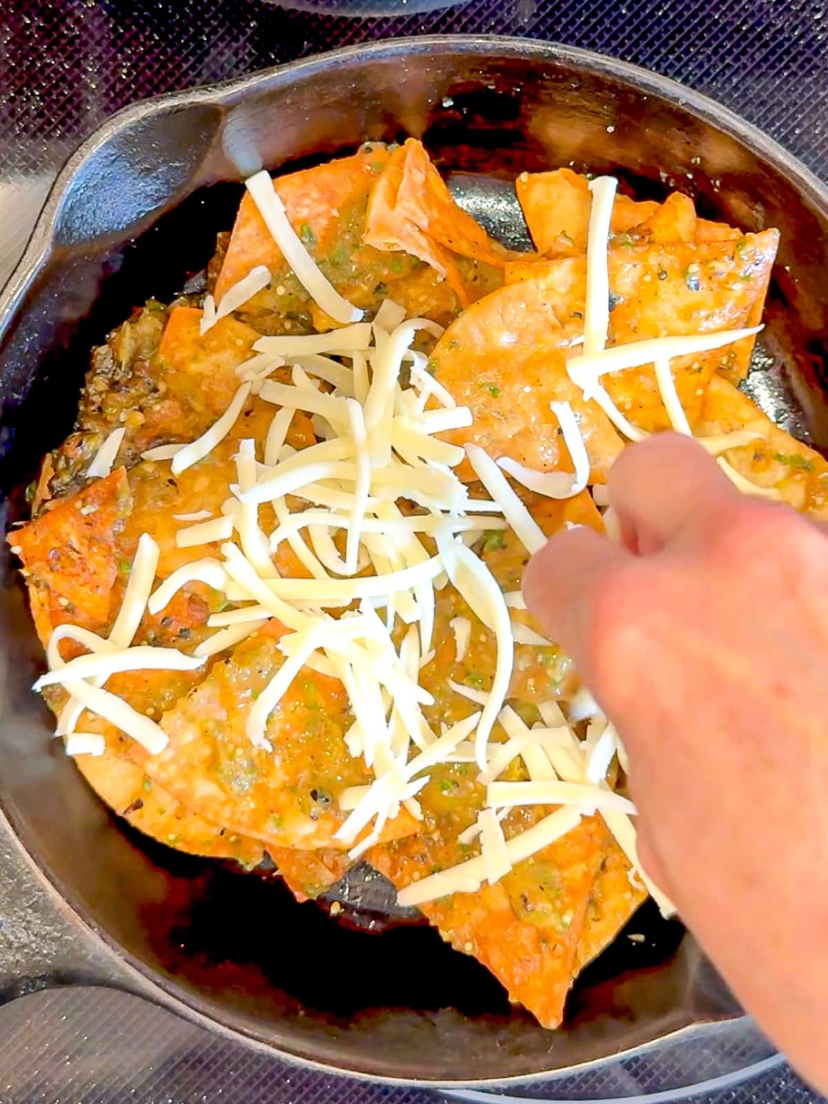 Adding shredded Monterey jack cheese to the top of tortilla chips tossed in salsa verde.