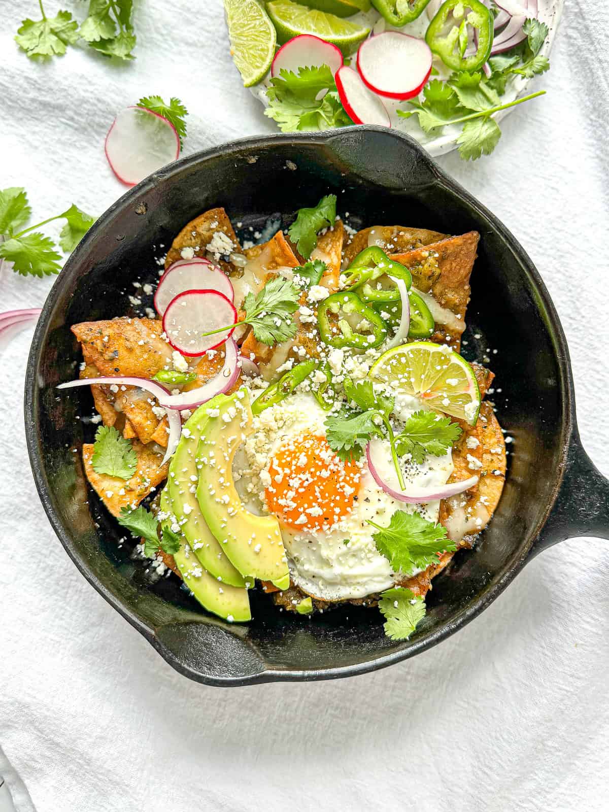 Breakfast Chilaquiles Verde in a cast-iron pan with an egg on it.