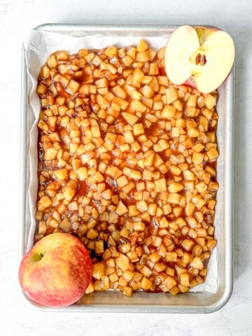 Sautéed maple apples on a sheet pan with two apples sliced open.