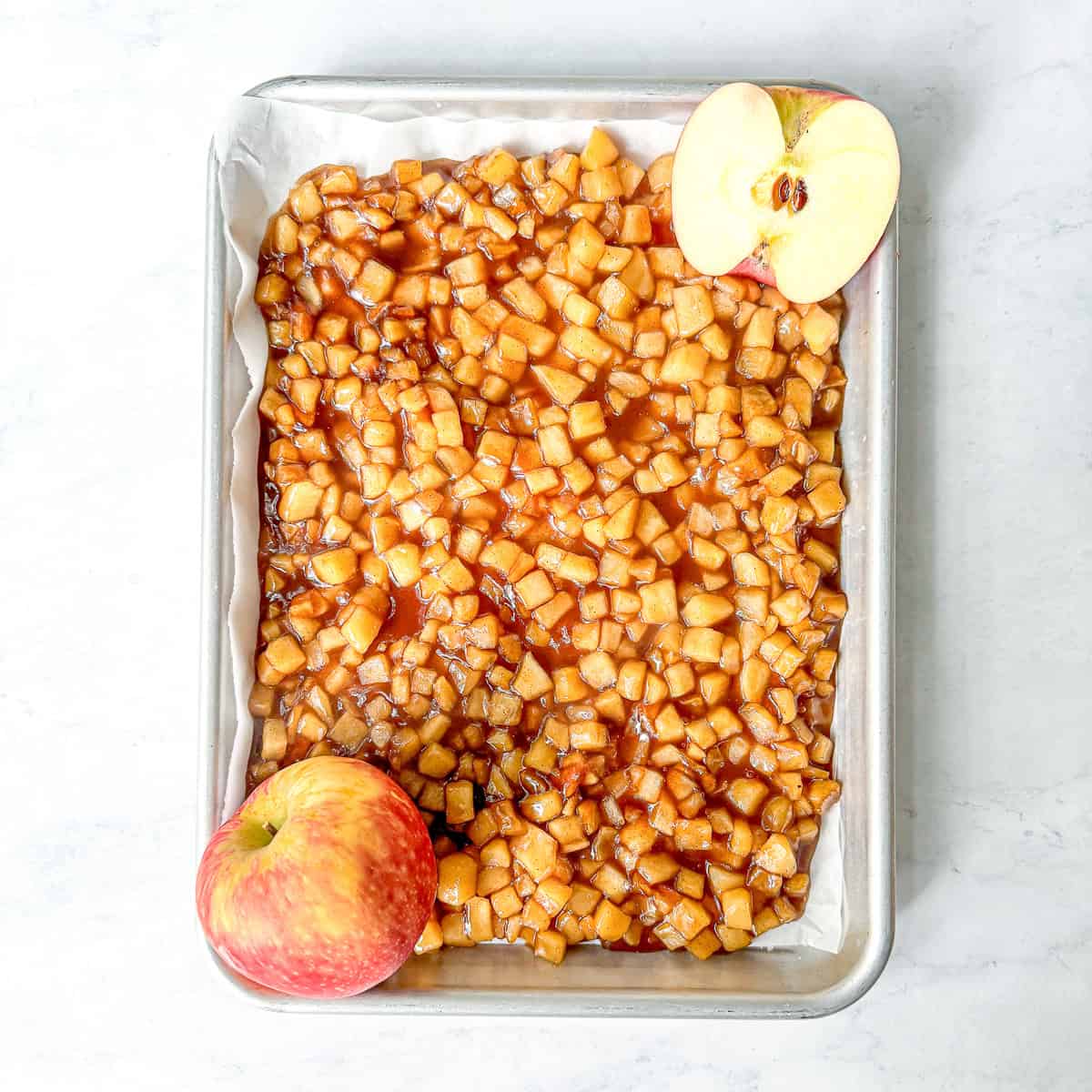 Sautéed maple apples on a sheet pan with two apples sliced open.
