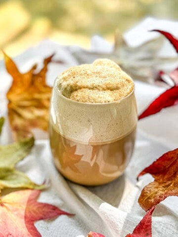 Pumpkin spice latte on a white tablecloth with a background of fall leaves.