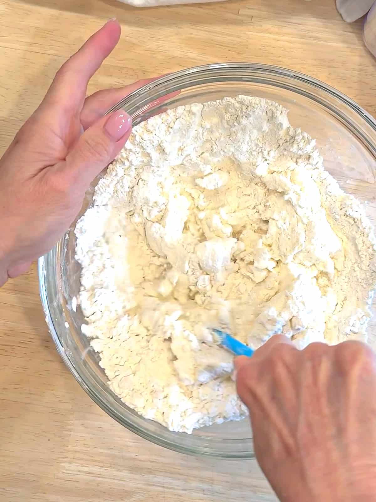 Mixing two ingredient dough in a glass bowl with a blue spatula.